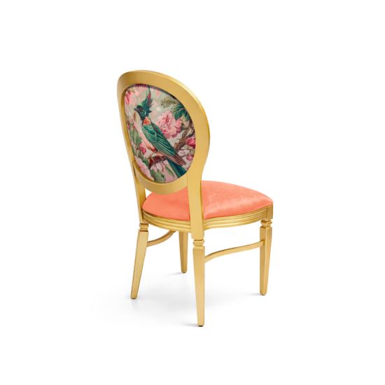 Gold dining chair with coral velvet seat and oval backrest featuring colorful bird and floral design for luxury event seating