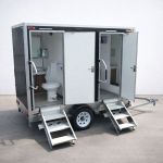 Luxury Portable RestroomBlack portable restroom trailer with dual doors, aluminum steps, diamond plate trim and tow hitch parked outdoors beside a swimming pool