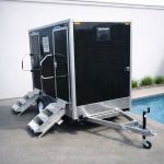 Luxury Portable RestroomBlack portable restroom trailer with dual doors, aluminum steps, diamond plate trim and tow hitch parked outdoors beside a swimming pool