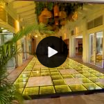 LED glass dance floor with purple glowing grid lights and reflective panels, modern light-up flooring priced per square foot for events.