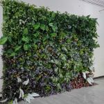 Lush green foliage wall backdrop with mixed leaves and floral accents, garden-style photo backdrop panel for weddings and events.
